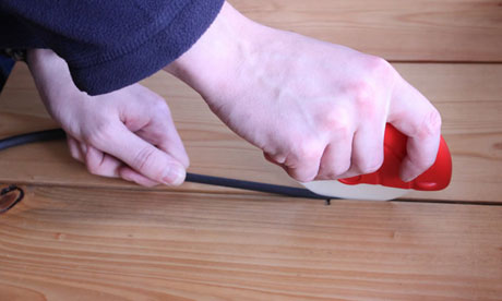 A pair of hands putting draught excluding tape between floorboards