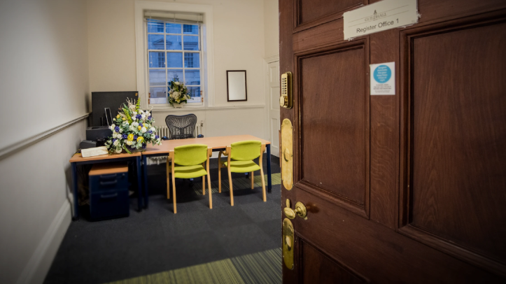 Registrar room with door open to the left and a desk and two green chairs in front of a desk